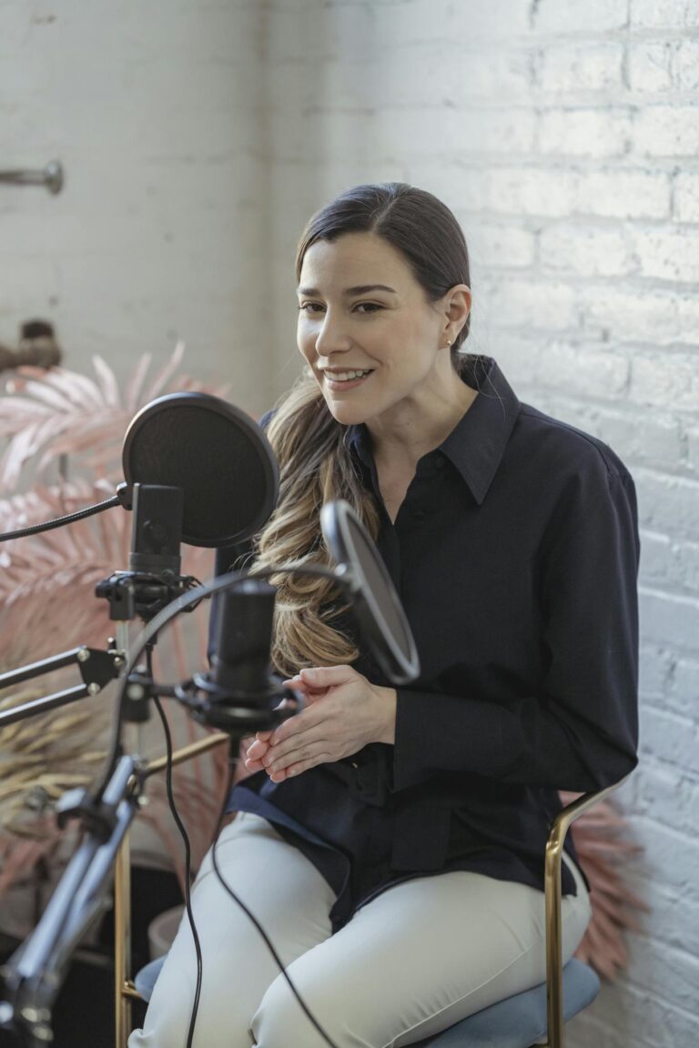 Young woman with a toothy smile recording a podcast at home, sitting indoors with a microphone.